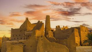 Ad Diriyah Heritage Tour with AMA Art Gallery and Al Awad Grand Mosque Visit An ancient, crumbling mud-brick city rises against a vibrant sunset sky, showcasing unique architecture and historical significance.