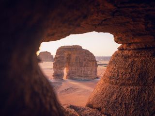 Saudi Arabia 9-Day Tour: Jeddah, Riyadh, Madain Saleh & Elephant Rock A monumental rock formation with an arch is framed by a cave entrance in a desert landscape, bathed in warm, golden light.