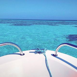 Yacht Charter and Cruise Expeditions Around the Kingdom A view from the bow of a boat, showcasing crystal-clear turquoise water and a serene blue horizon.