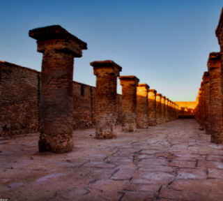 Tour from Dammam Area to the Oldest Port on the Maritime Arabian Silk Road Here's a one-sentence description of the image:A long row of ancient stone columns with square capitals lines a weathered, paved pathway under a clear blue sky.