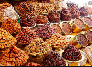 Riyadh Food, Coffee, Tea, and Snacks Tour This image shows a vibrant display of dates in various types and colors, arranged in piles and containers at a market stall, creating a rich, diverse, and appealing assortment.