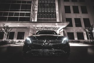 Saudi Arabia Luxury Car Rental: Rolls-Royce, Ferrari, Porsche and More A Mercedes-Benz SUV is parked in front of a modern building at night with headlights illuminating the scene.
