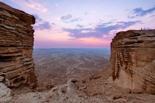 Edge of the World Day Tour from Riyadh A vast desert landscape framed by towering rock formations under a pastel sky.