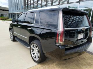 Saudi Arabia Premium SUV Rental with Expert Driver A black Cadillac Escalade SUV is parked on a concrete surface in front of a modern building with reflective glass windows.